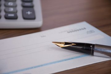 Mock up image of cheque book, pen and calculator on wooden background.