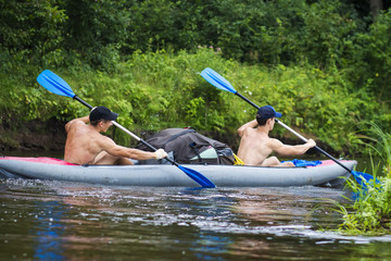Two young sports guy in a boat rowing oars on the water. Kayaking along the river in the summer...