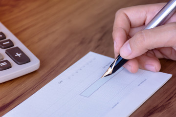 Woman hand writing cheque book on wooden table background.