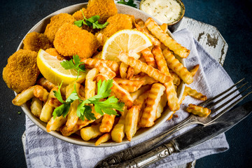 English traditional fast food, junk food, British dish Fish and chips with tartar sauce, lemon and greens, on a dark blue background, copy space above