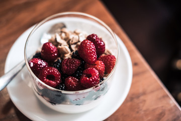 Yogurt with granola, raspberries on wooden coffee table. Hipster coffee shop. Food photography concept. Image filter tones. Copyspace