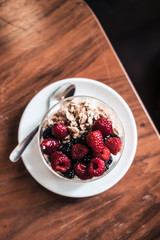 Overhead yogurt with granola, raspberries on wooden coffee table. Hipster coffee shop. Food photography concept. Image filter tones. Copyspace