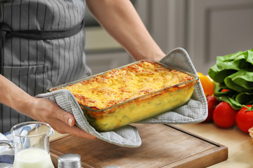Woman holding baking tray with spinach lasagna in kitchen