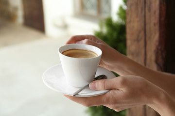 Young woman with cup of delicious coffee on blurred background