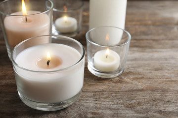 Fototapeta na wymiar Burning wax candles in glasses on wooden table