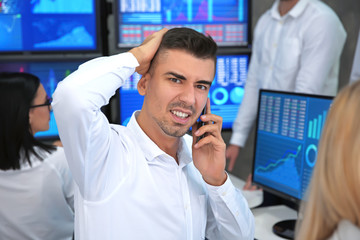 Displeased male stock trader talking by cellphone on office