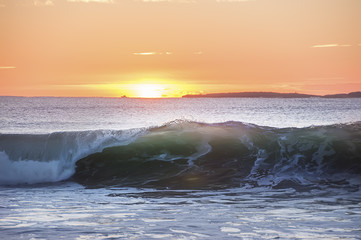 early morning on the shore of the Atlantic Ocean. A wave rolling on the shore in the sunlight. ...
