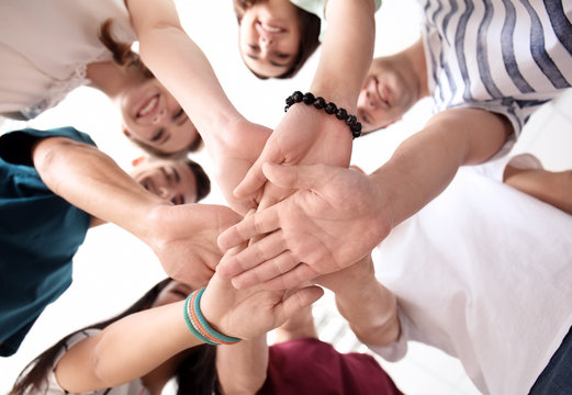 People putting hands together indoors, view from below. Unity concept