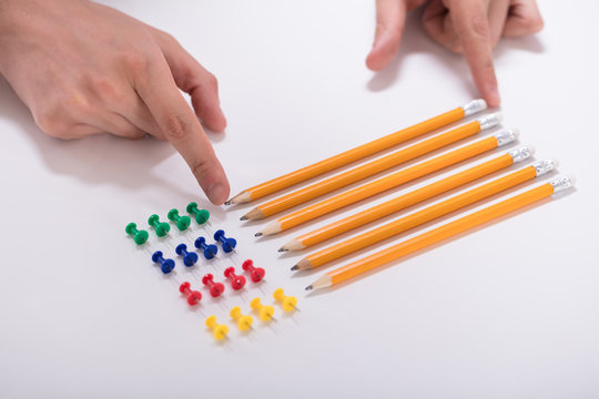 Person's Hand Arranging Pencils And Multi Colored Pushpins