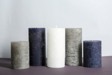 Different decorative wax candles on table against light background
