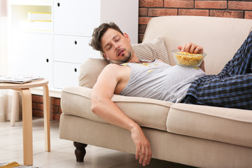 Lazy man with bowl of chips sleeping on sofa at home
