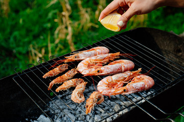Langoustine and shrimp are grilled. The woman turns the shrimps forceps with chef tongs, sprinkles them with half-lemon juice