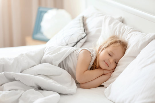 Cute little girl sleeping on bed with soft pillows at home