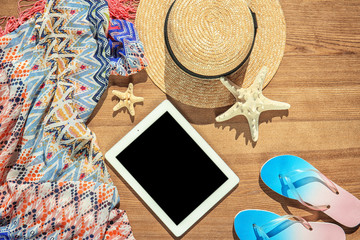 Flat lay composition with tablet and beach objects on wooden background