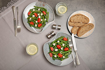 Plates with tasty green beans, tomatoes and cheese on table, top view