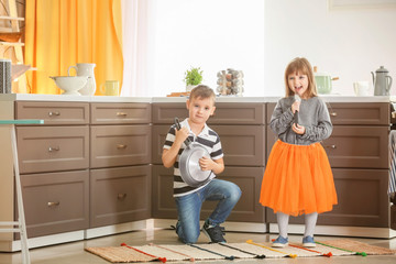 Cute little children playing as musical band in kitchen
