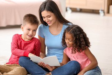 Young woman reading book to little kids indoors. Child adoption