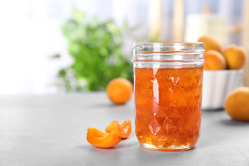 Jar with tasty apricot jam on table