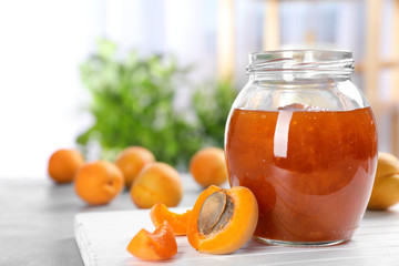 Jar with tasty apricot jam on wooden board