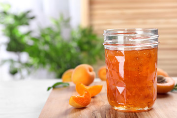 Jar with tasty apricot jam on wooden board