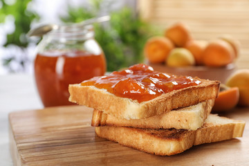 Bread with tasty apricot jam on wooden board