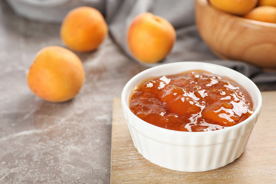 Bowl with tasty apricot jam on wooden board