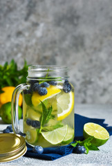 Lemonade with lime, lemon and blueberries on a stone background. Summer cold drink.