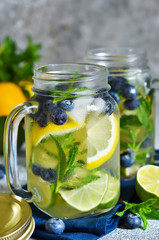Lemonade with lime, lemon and blueberries on a stone background. Summer cold drink.