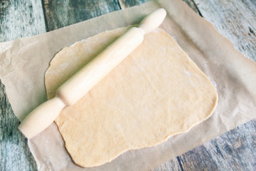 Dough with rolling pin on a baking paper on wooden background