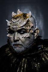 Demon with golden collar on black background. Man with thorns or warts, face covered with glitters....