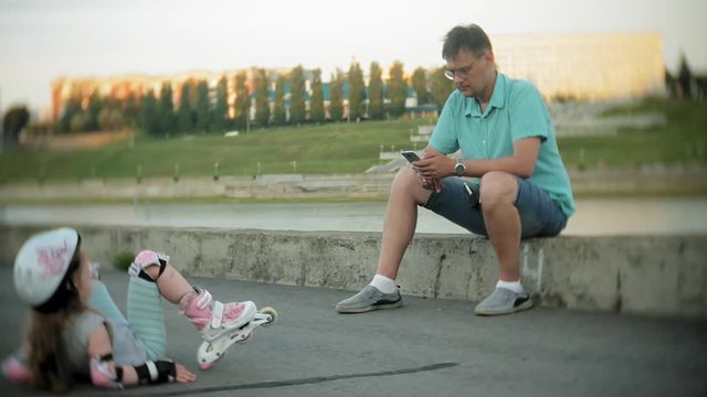 father and daughter ride on roller skates. Girl learning to roller skate, and falls. father teaches daughter to ride on rollers