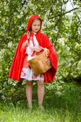 Smiling blond girl posing in a dress of little red riding hood near green trees