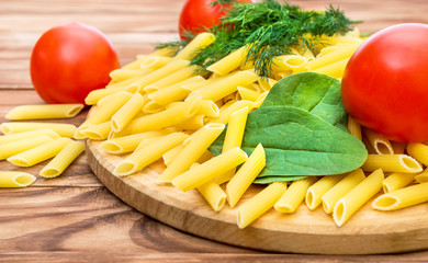 Cutting board with raw pasta, tomatoes, spinach and dill on wooden table. Cooking food.