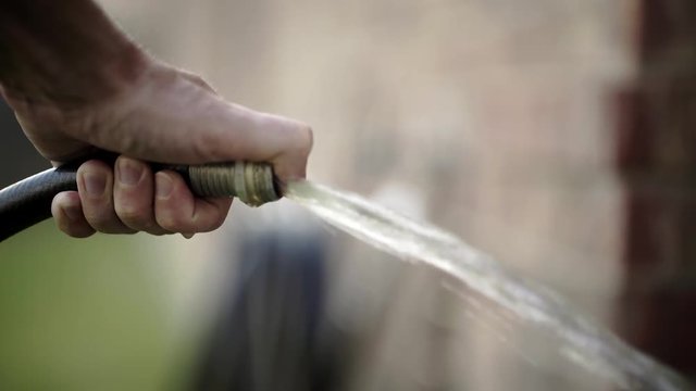 Close up of a hand spraying water from a water hose using a thumb on the spout.