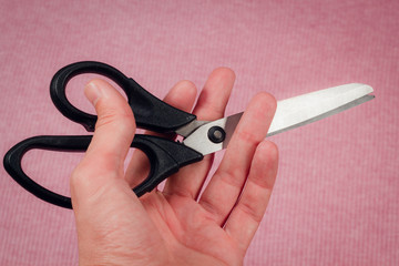 Scissors in hand on pink fabric background.