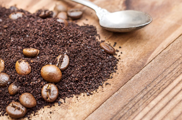 Heap of ground coffee and coffee beans with spoon on the table.