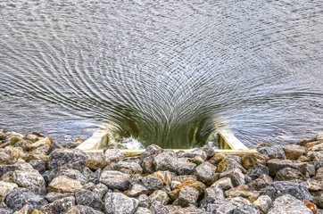 Strong current in a river towards a culvert in a dike