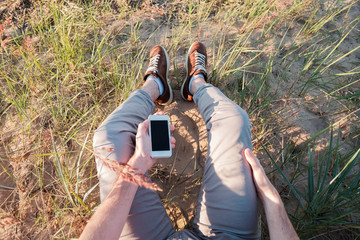 Outdoor photo of man sitting on grass holding phone with blank screen.