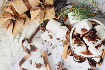 Winter Christmas New Year hot warming drink. Cup of hot chocolate or cocoa with marshmallow, gift boxes with ribbon, fir branch, star anise, cinnamon on white knitted background