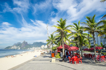 Bright morning view of a kiosk and palm trees on the Ipanema promenade with the beach and two brothers mountain backdrop.