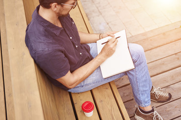 Man reading book sitting outside in public space. Wearing glasses alone working. Concept of education or busyness.