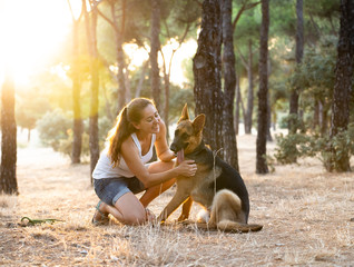 Young attractive latin woman teaching and loving her beautiful cute german shepherd dog in the park at sunset in nature care support happiness peaceful friendship training animals lifestyle concept.