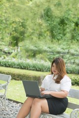 Pretty Asian fat woman pose working with laptop on a chair in the park.
