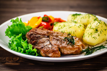 Grilled steak, baked potatoes and vegetable salad on wooden background 