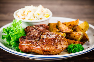 Grilled steak with baked potatoes and vegetables served on wooden table 