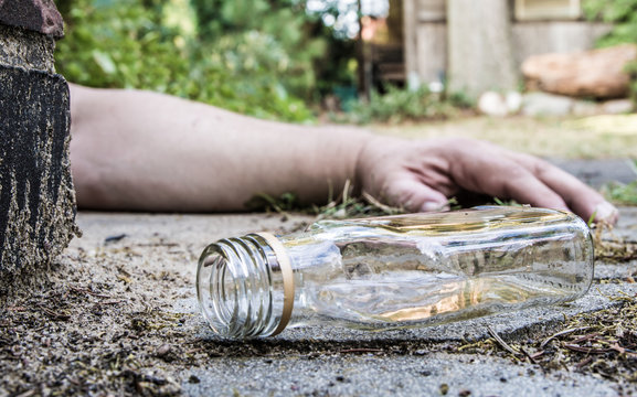 ein alkoholkranker Mann und eine leere Schnapsflasche liegen auf der Strasse
