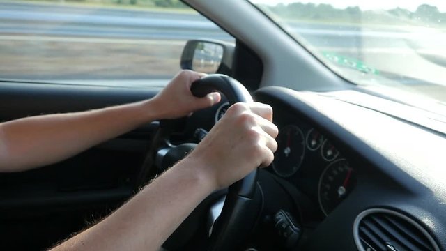 Hands on steering wheel man driving a car on highway in sun light haze