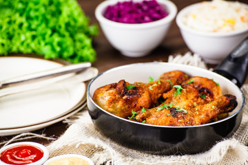 Fried drumsticks in pan with vegetables on wooden table