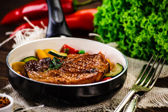Grilled steak with vegetables in pan on wooden table