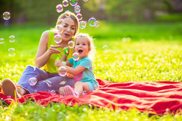 Happy family in park -Female child blows soup foam and make bubbles with her mother in nature.